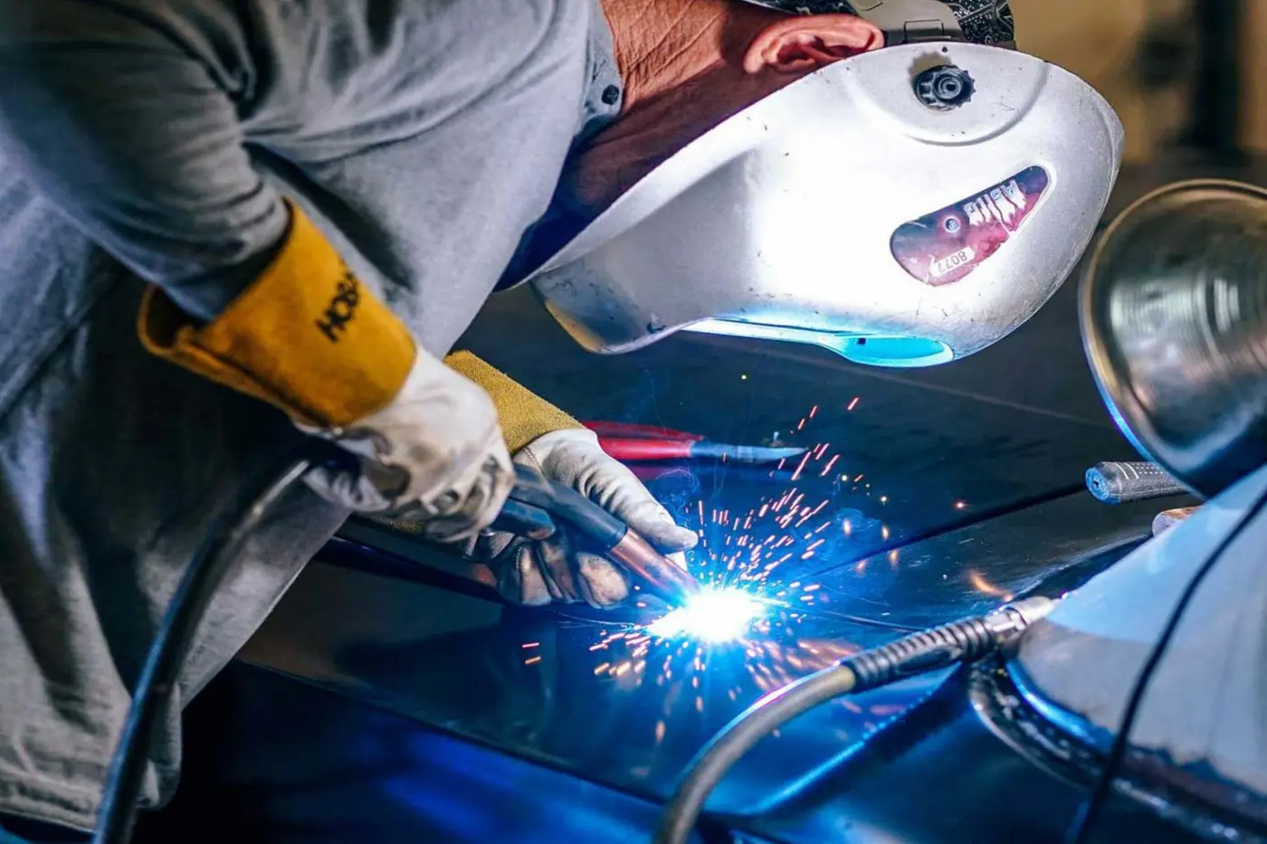 Welding specialist working with sparks on a vehicle body panel at C.A.M.S. Chippenham